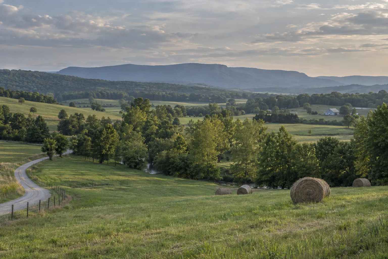 Rolling green farmland with round hay bales and a long plateau on the horizon